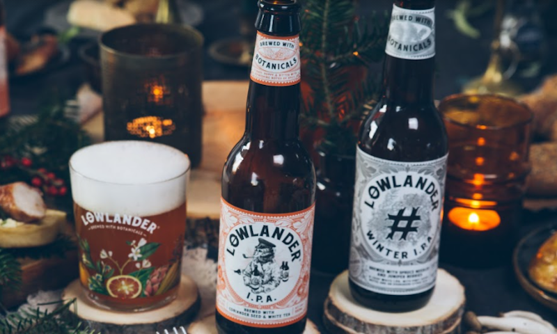 Twee flesjes Lowlander bier op tafel met een glas en kaarsjes ernaast 